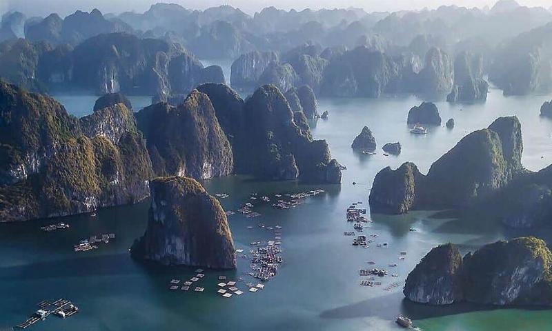 kayakers paddling through emerald waters among towering limestone karsts in Lan Ha Bay